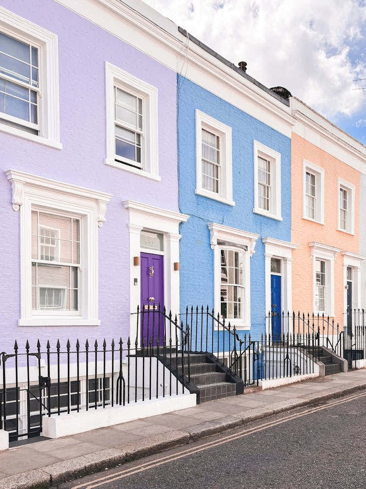 London, England I Pastel facades of Notting Hill streets captured in colorful British architecture photography to the purple blue and pink dollhouse aesthetic of an everyday lifestyle londoner street scene