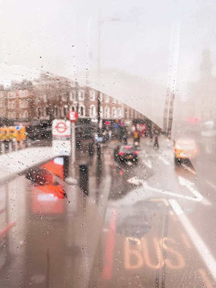London, England I View of a rainy street through the fogged window of a legendary red London bus capturing nostalgic atmosphere photography and vibrant colors of the city in the rain with grey moody aesthetic