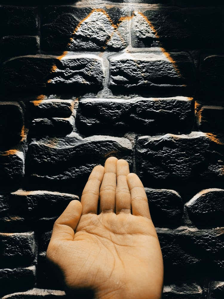 Hand Reaching Up To A Brick Wall