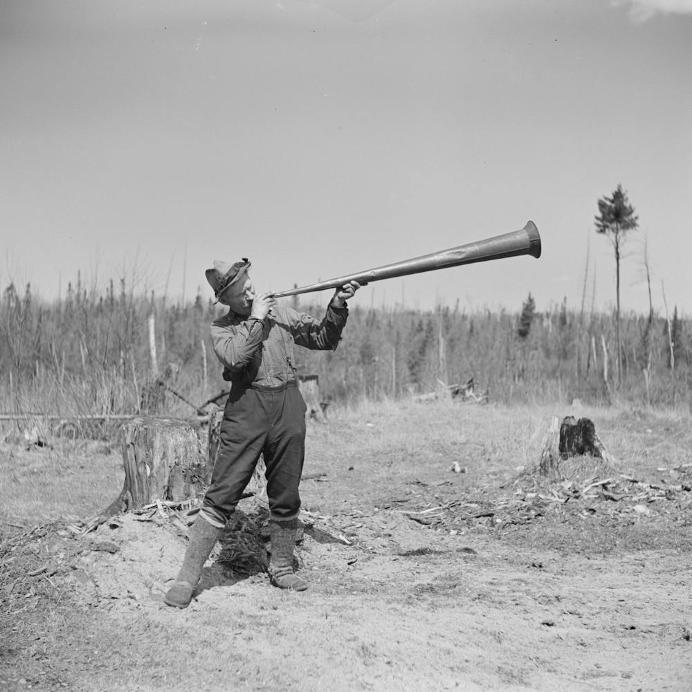 Lon Allen, Former Lumberjack, Now A Cut Over Farmer, Demonstrates How Cooks Used Horn To Call Jacks To Dinner