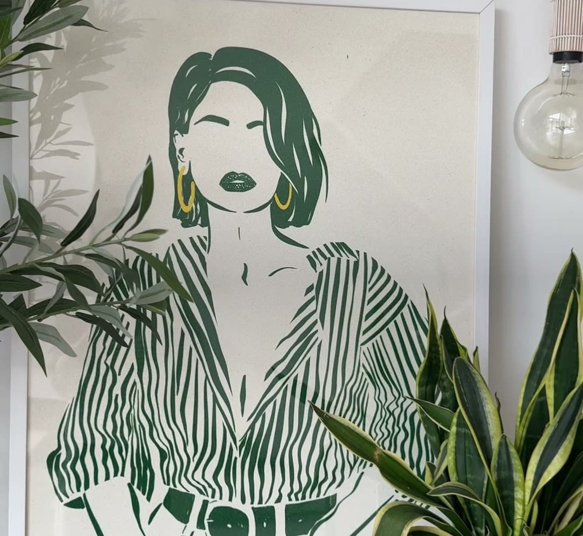 Green line-art portrait print being hung beside an olive tree