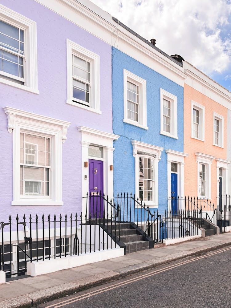 London, England I Pastel facades of Notting Hill streets captured in colorful British architecture photography to the purple blue and pink dollhouse aesthetic of an everyday lifestyle londoner street scene
