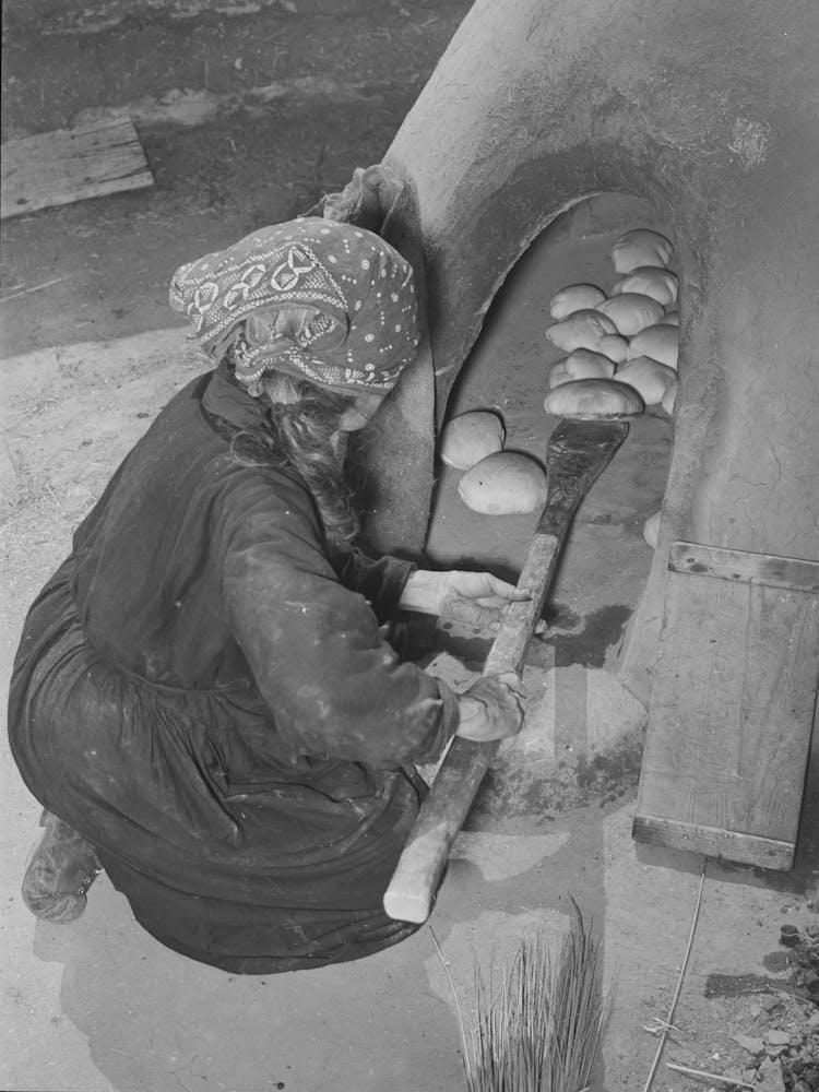 Spanish American Woman Removing Baked Bread From Outdoor Earthen Oven By Means Of A Long Wooden Paddle