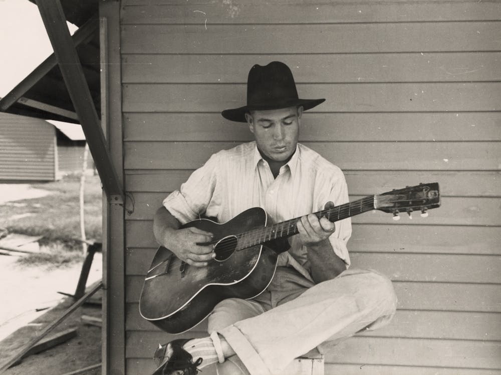 Migratory Worker Playing Guitar On Front Porch Of His Metal Shelter In The Agua Fria Labor Camp, Arizona By Russell Lee