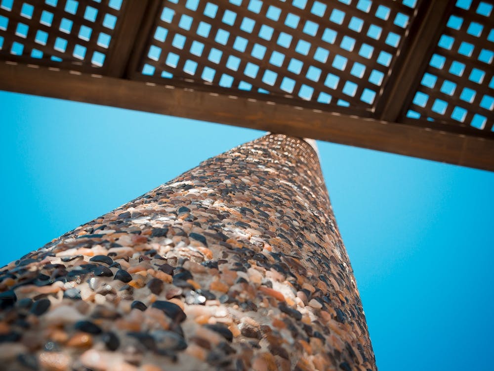Low Angle View On Wooden Shade Of Seating Bench With Pebble Stone Column
