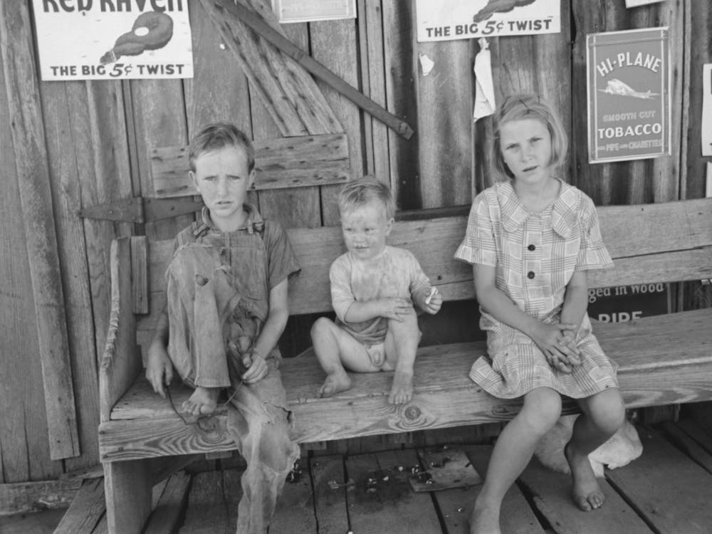 Children Of Agricultural Day Laborers Sitting On Bench In Front Of Small Store Near Vian, Oklahoma By Russell Lee
