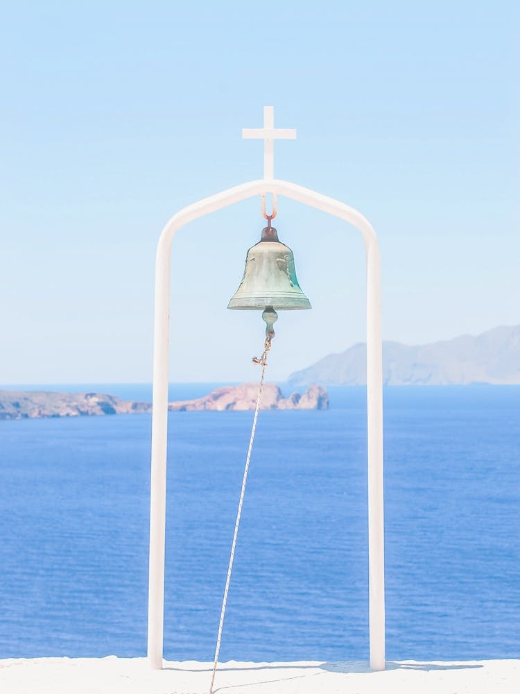 Milos, Greece I The church, its bell, its cross over Mediterranean sea and blue white architecture with a minimalist geometric mountain panorama photography and summer pastel aesthetic from Cyclades islands