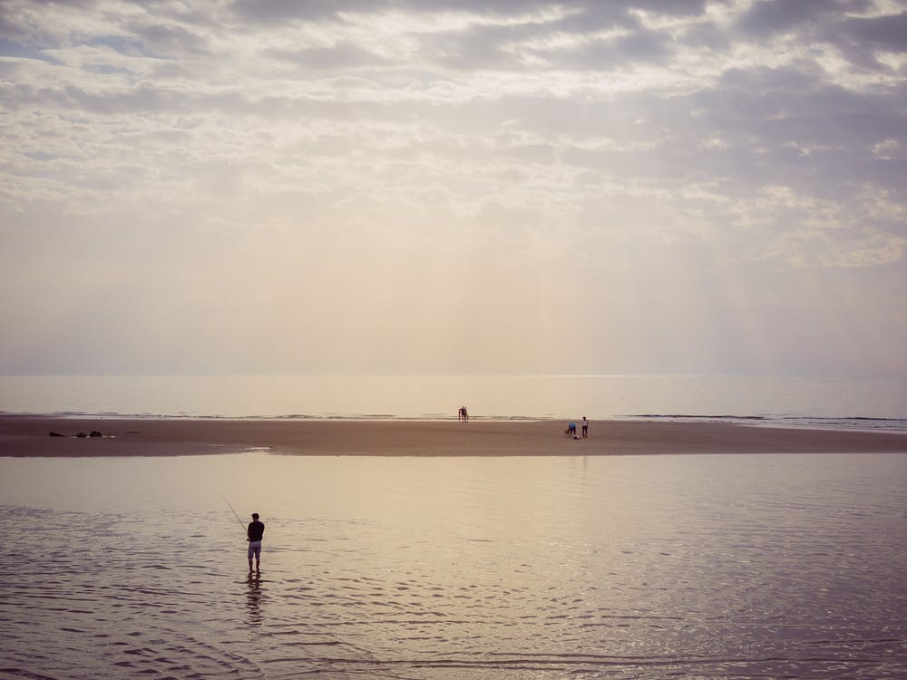 People Doing Various Activities Along The Shore Of The Beach At Sunset