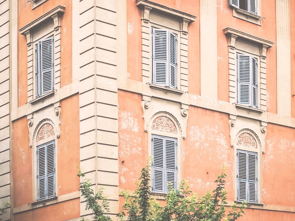 Rome, Italy I Light orange facade of a weathered Italian building with blue shutters with geometric and authentic architecture photography in pastel aesthetic capturing the charm of la dolce vita
