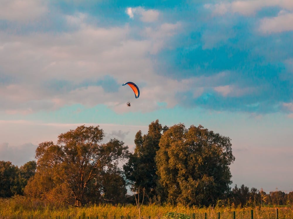 Motorisierter Gleitschirmflieger fliegt bei Sonnenuntergang über ländliche Gegend