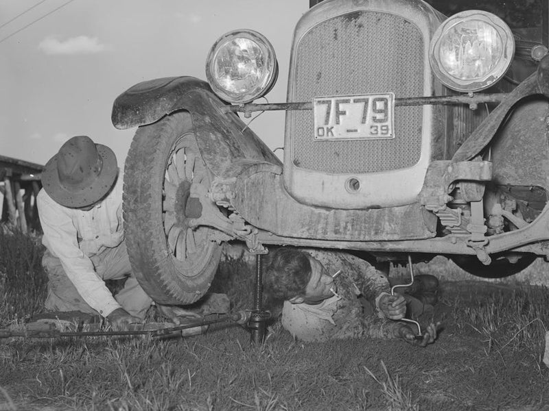 Migrant Steeple Jack Removing The Crank Case From His Automobile While His Father Blocks Up The Front Wheel, Near Pragu