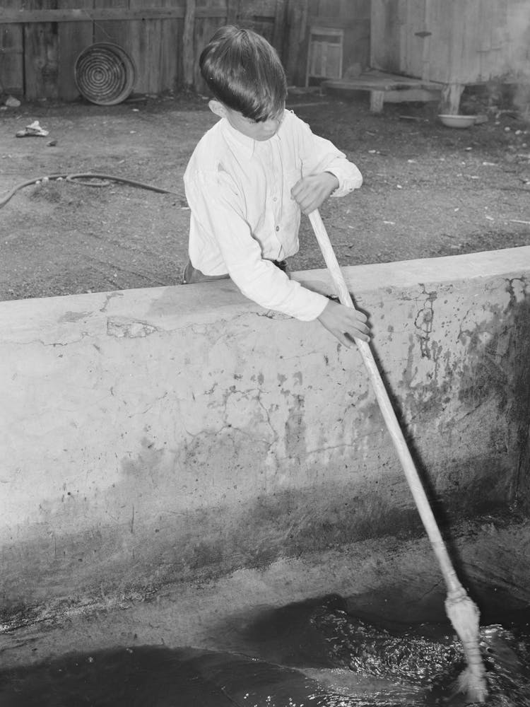 Mexican Boy Sweeping Out Vat In Which Pecans Are Soaked Before Cracking, They Must Be Damp To Prevent