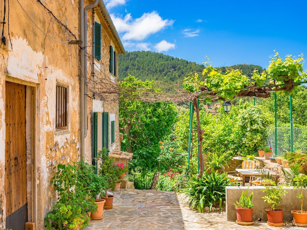 Mittelmeer Spanien. Im bezaubernden alten Dorf Valldemossa auf der idyllischen spanischen Insel Mallorca erwartet Besucher eine malerische Szene. Traditionelle Blumentöpfe schmücken die Wände der engen Gassen und Wohngebäude und bringen Farbe und