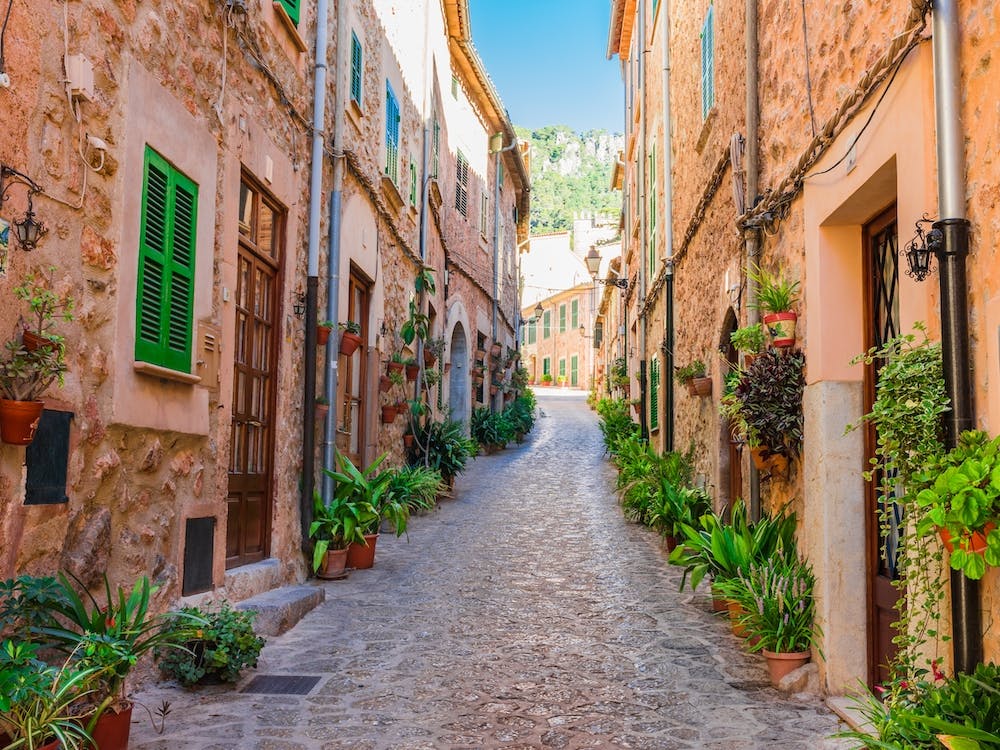 Beautiful street at the mediterranean village of Valldemossa on Majorca Spain. Wander through beautiful streets lined with historic buildings adorned with blooming flowers and lush plants. Admire the intricate architecture and facades of the old houses, and feel the romance in the air.