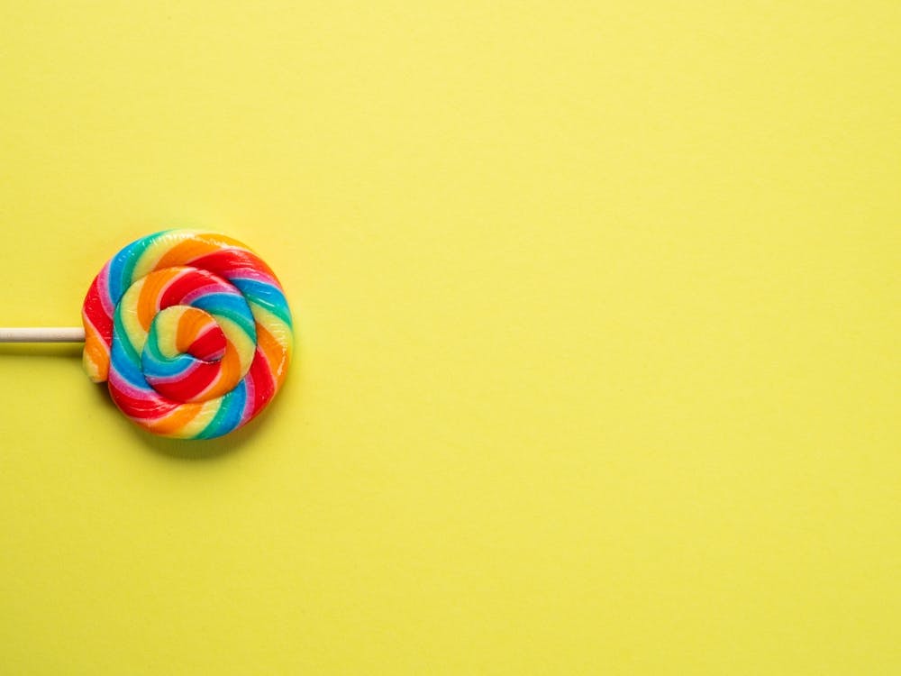 Popart rainbow lollypop - colorful candy on a yellow backdrop - fun food photography by Christa Stroo Photography