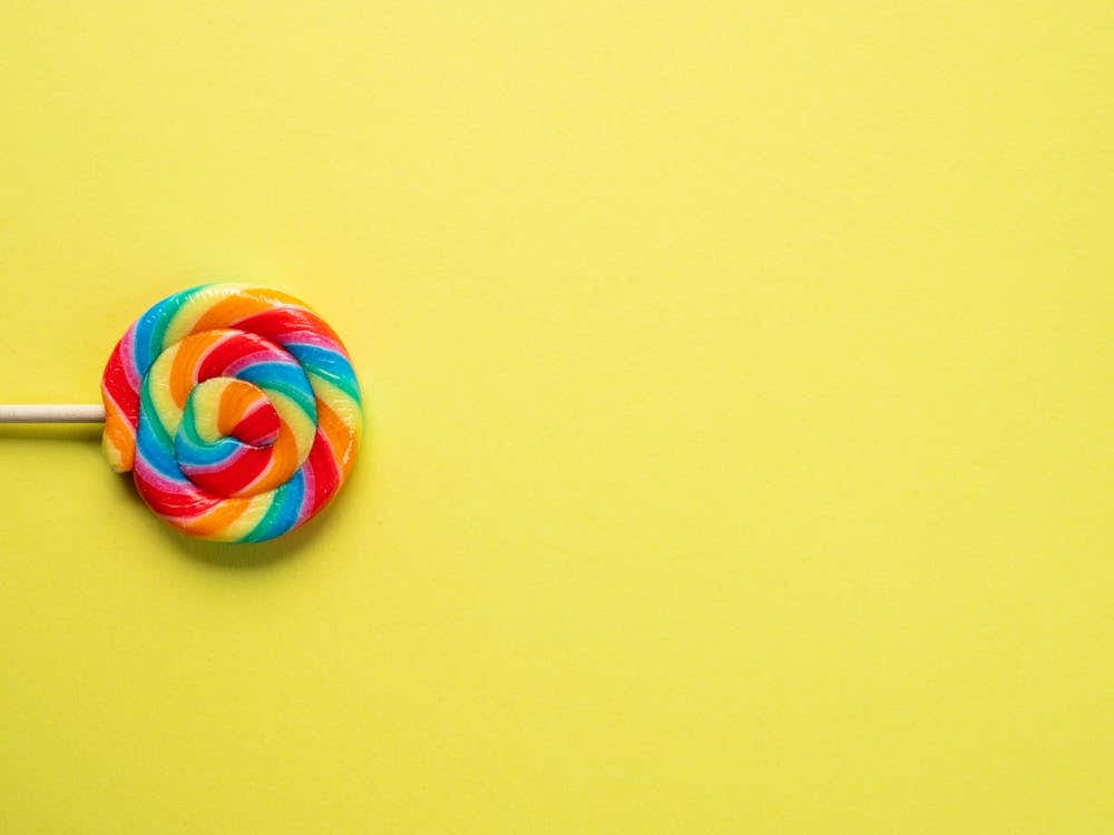 Popart rainbow lollypop - colorful candy on a yellow backdrop - fun food photography by Christa Stroo Photography