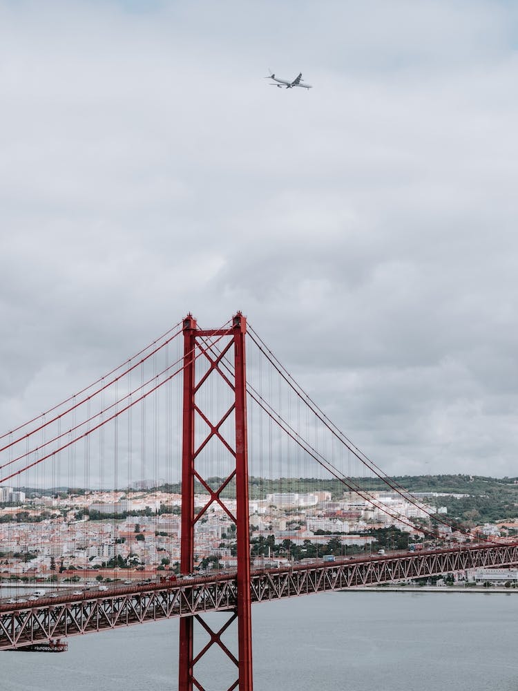 The 25 de Abril Bridge with an airplane flying over it.