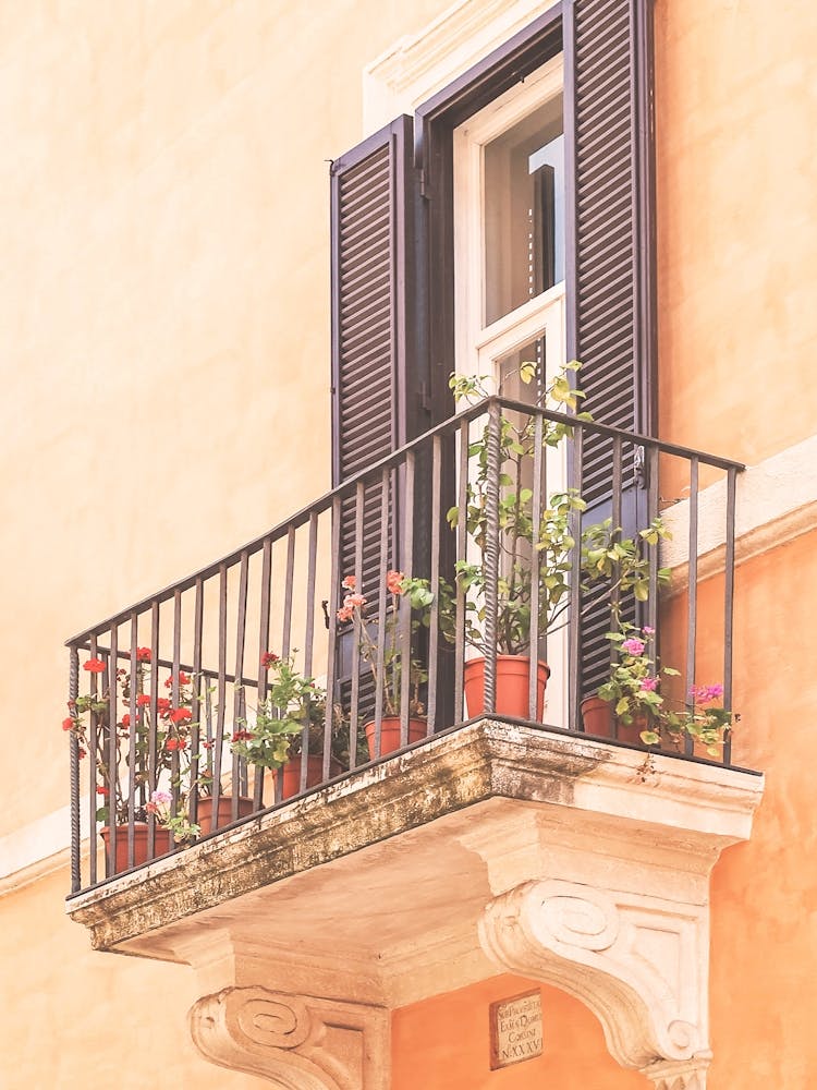 Rome, Italy I Flowered balcony and window on orange pastel facade in summer light with minimalist geometric urban architecture photography capturing the soft authentic charm of Italian la dolce vita