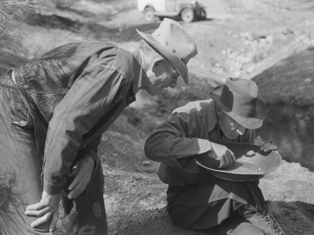 Gold Prospector Blowing Away Dirt To Find The Gold In His Pan While A Visiting Prospector Looks On, Pinos Altos, New
