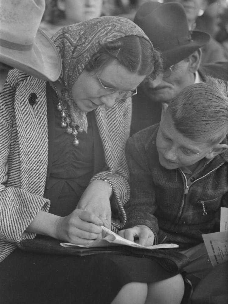 Spectators At The Rodeo Looking At The Program, San Angelo Fat Stock Show, San Angelo, Texas By Russell Lee