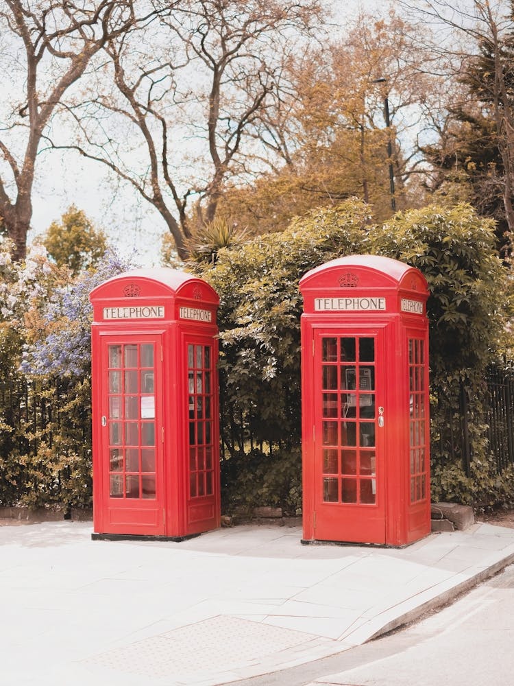 London, England I Iconic vibrant red British telephone boxes in Primrose Hill londoner district street photography of an urban scene in a natural park with autumn pastel retro vintage aesthetic