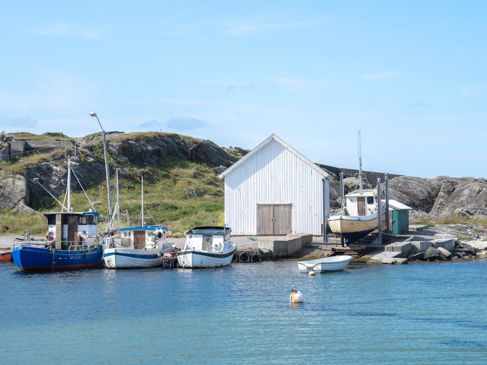 A white boathouse en some fishing ships in a small harbour at Ølberg in Norway - summer nature and travel photography by Christa Stroo