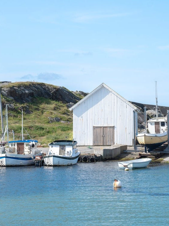 A white boathouse en some fishing ships in a small harbour at Ølberg in Norway - summer nature and travel photography by Christa Stroo