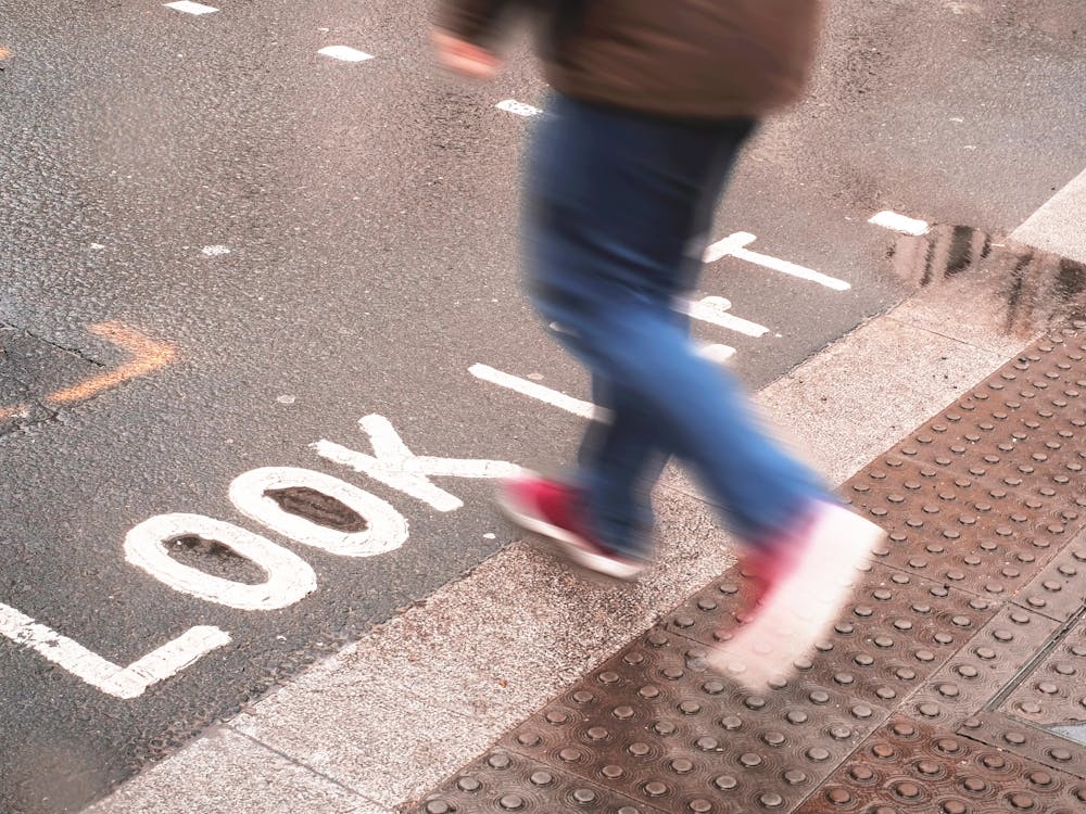 London, England I Pedestrian in motion on a crossing with Look Left inscription on the ground under the rain in the urban dynamic of a London street photography with a retro vintage autumn aesthetic