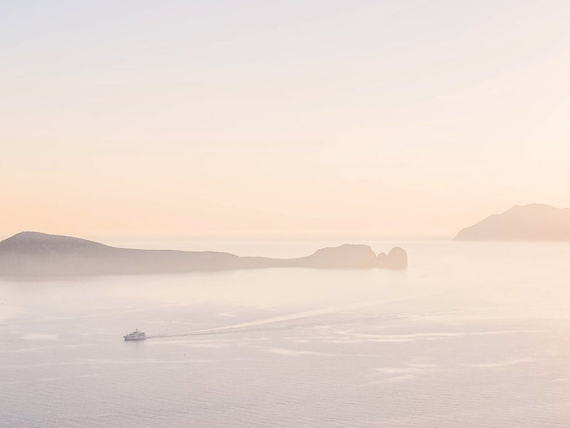 Milos, Greece I Summer pastel aesthetic sunset over the mountains and a boat on Mediterranean sea for a minimalist fine art photography of soft soothing calming nature in pink orange retro tones