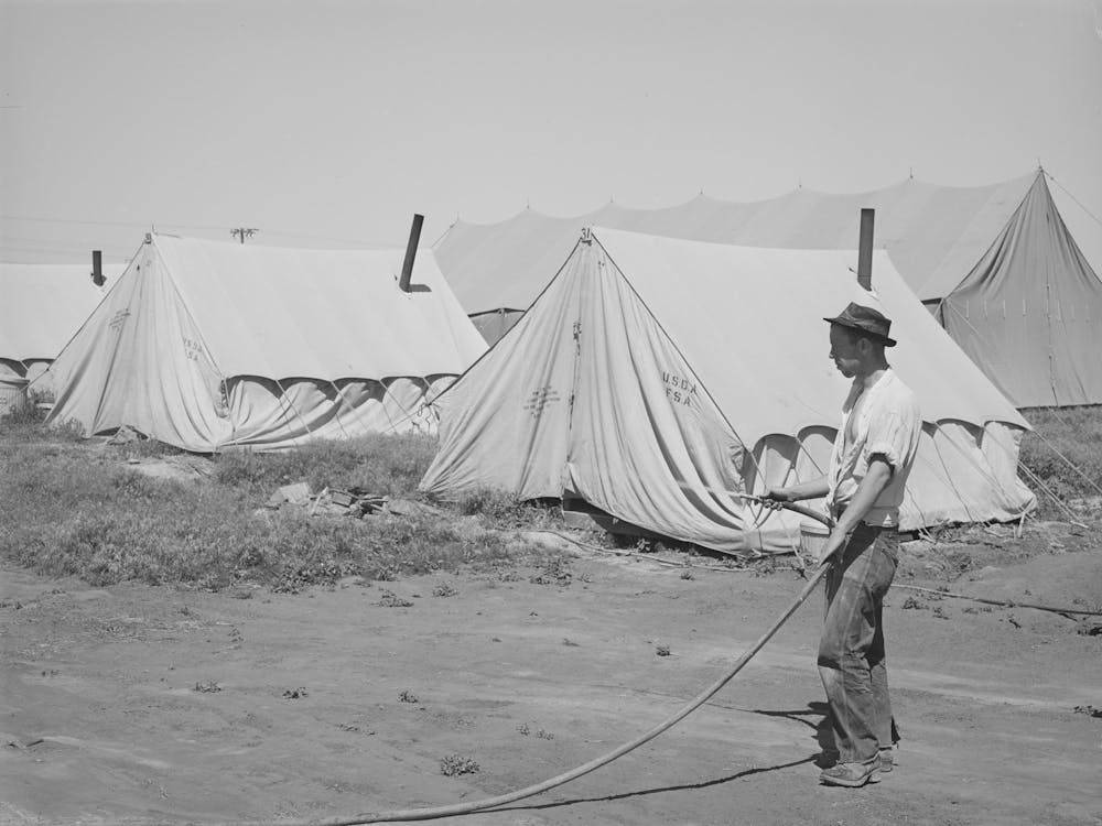 Farm Worker Watering Down The Dusty Ground Around His Tent At The Fsa (Farm Security Administration) Migratory Lab
