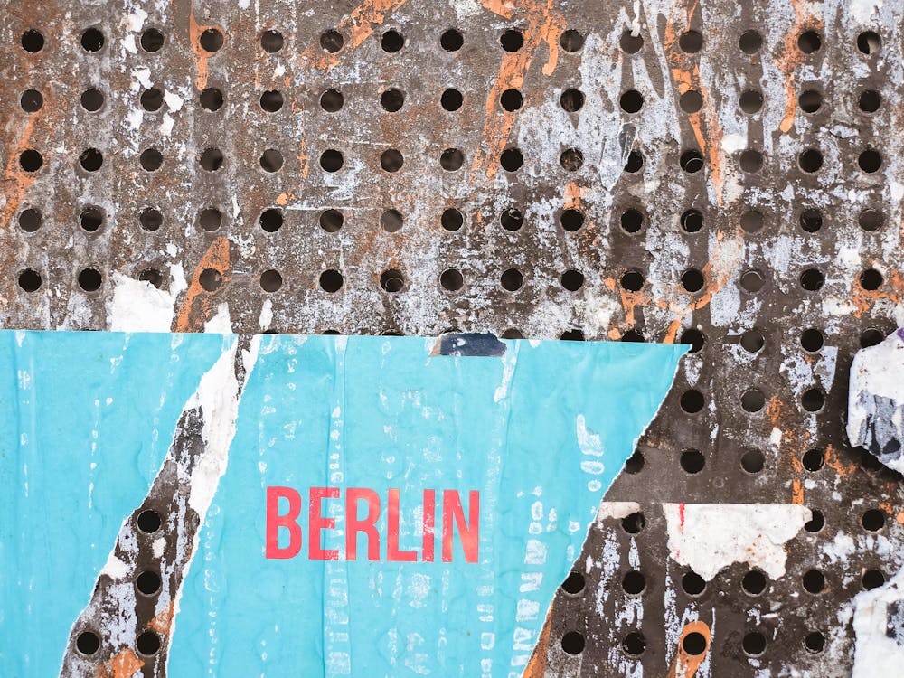 Berlin, Deutschland I Zerrissenes urbanes Poster auf perforierter Metallwand mit kräftiger Typografie auf blauem Hintergrund mit roher Street-Art-Ausstrahlung, urbaner Stadtgrafik-Underground-Ästhetik-Fotografie und Pop-Farbenergie