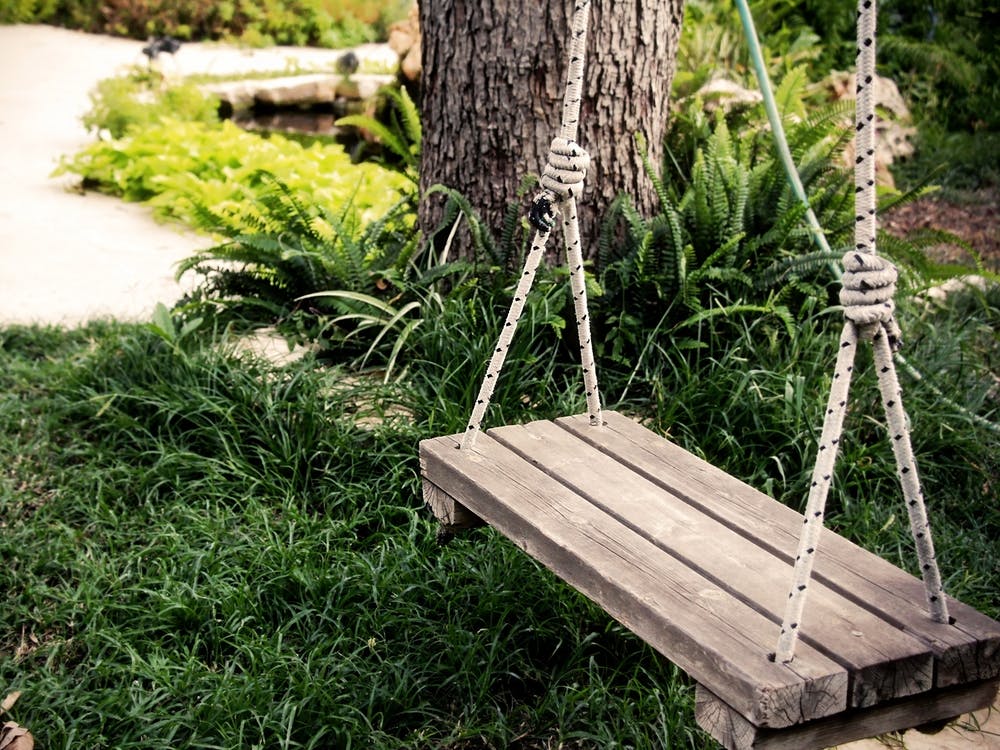 Old Wooden Vintage Swing Hanging From A Large Tree In The Garden With Green Grass Background