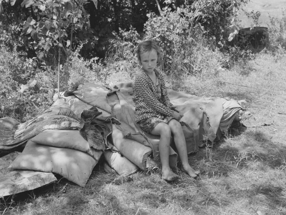 Child Of Family Encamped By The Roadside Sitting On Bedclothing, There Were No Beds And No Overhead Coveri