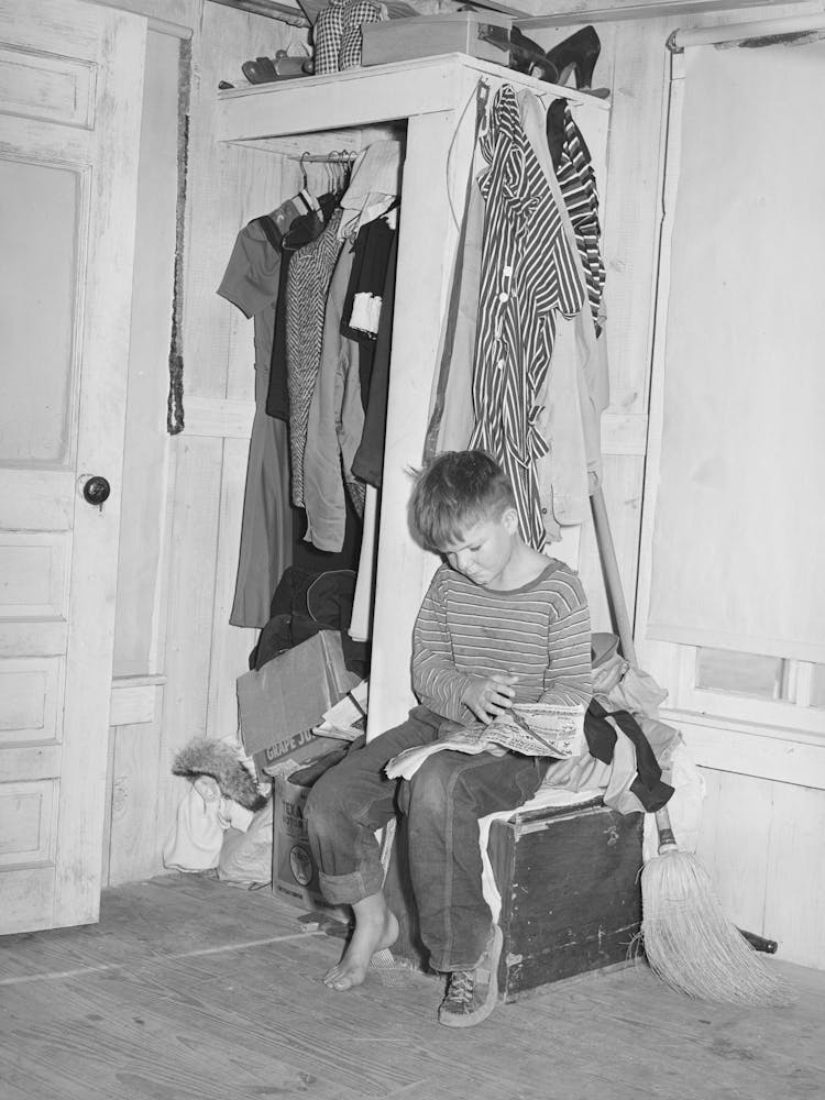 Small Boy, Son Of Carpenter From Hobbs, New Mexico, Reading Funny Papers In Corner Of Room In Tourist Court