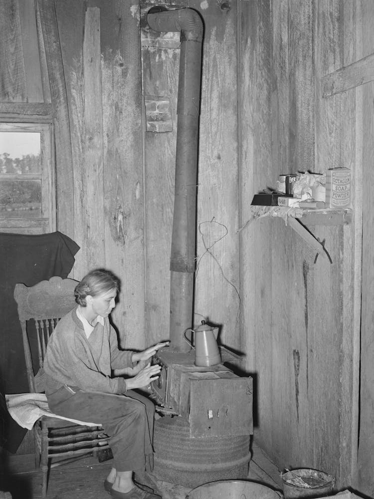 White Migrant Berry Picker Warming Her Hands Over A Makeshift Stove Constructed By Her Husband