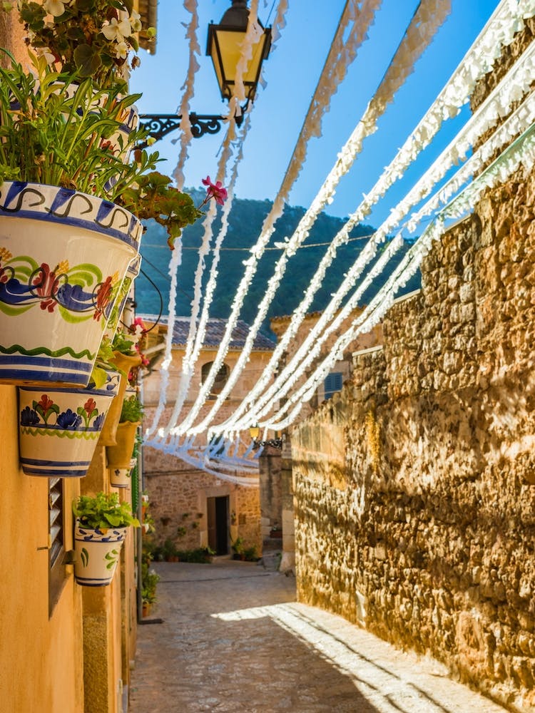 Spain, Valldemossa fiestas, lose yourself in the narrow, rustic streets of Valldemossa, a charming old village in Mallorca, Spain. Admire the Mediterranean stone buildings adorned with potted plants and flowers, showcasing the rich Balearic Island culture