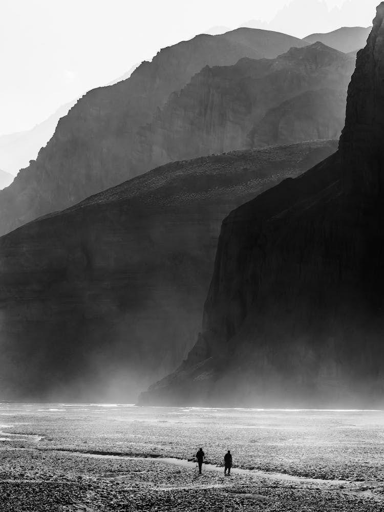 Two People Walking Through A Riverbed In The Himalayas