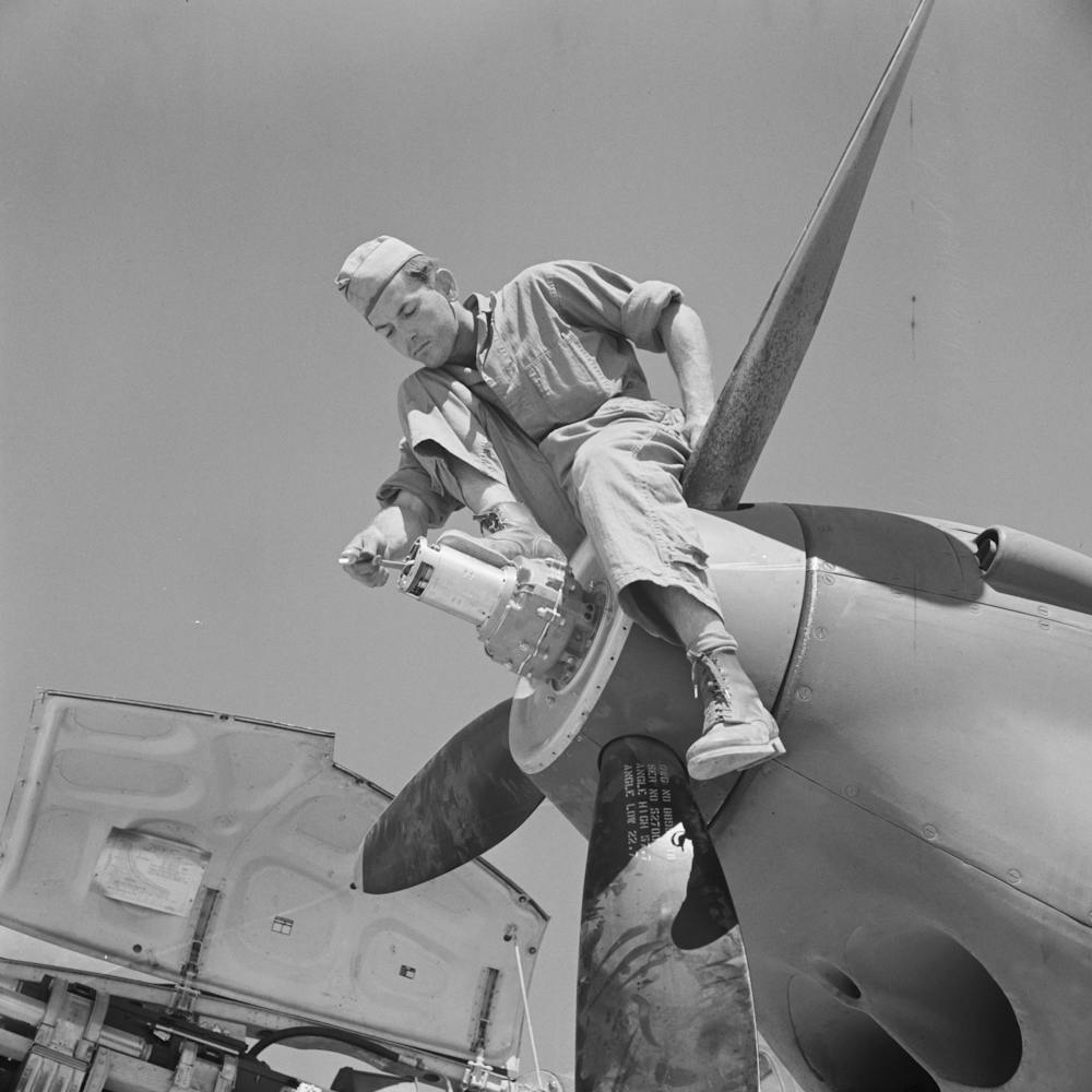 Repair Man Perched Upon Propeller Hub Of Airplane, Lake Muroc, California By Russell Lee