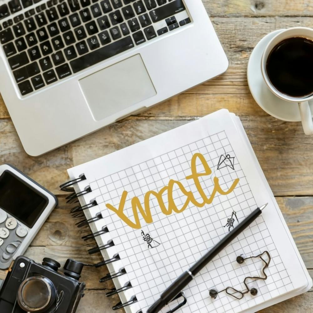 An overhead shot of a well-organized and visually appealing desk with a laptop, notebook, and a cup of coffee, representing productivity and a conducive work environment. This image can be applied across various industries for website banners, social media posts, or marketing materials