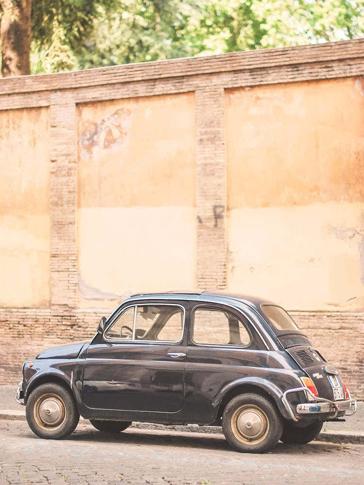 Rome, Italy I Vintage italian car in quiet street with soft orange city wall for a charming urban photography scene with pastel aesthetic tones with retro vibes and authentic dolce vita atmosphere