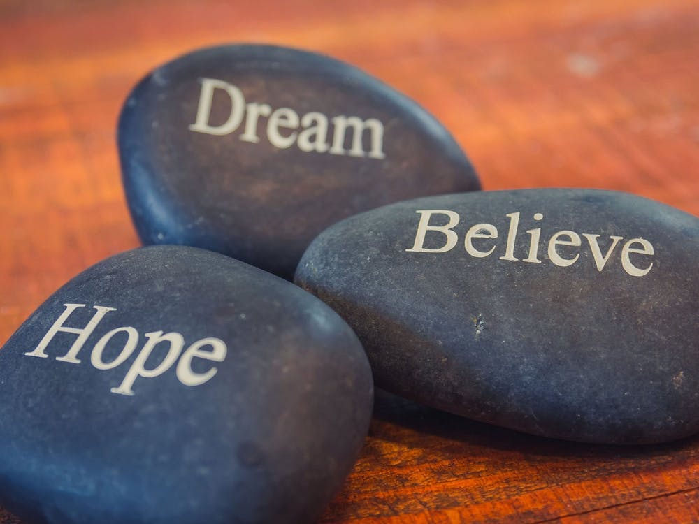 Black Inspirational Pebble Stones With The Words Dream, Believe And Hope On Wooden Background