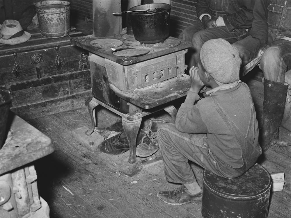 Boy Sitting By The Stove On A Cold Day In The Strawberry Picking Season, Near Independence, Louisiana By Russell Lee