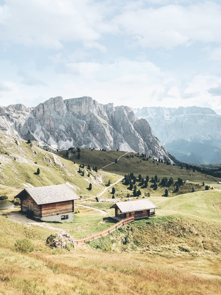 Dolomites, Italy I Picturesque wooden chalets photography in the green Seceda mountains of an Alps landscape between lush green meadows, fir forests and pastel blue summer skies of preserved peaceful nature