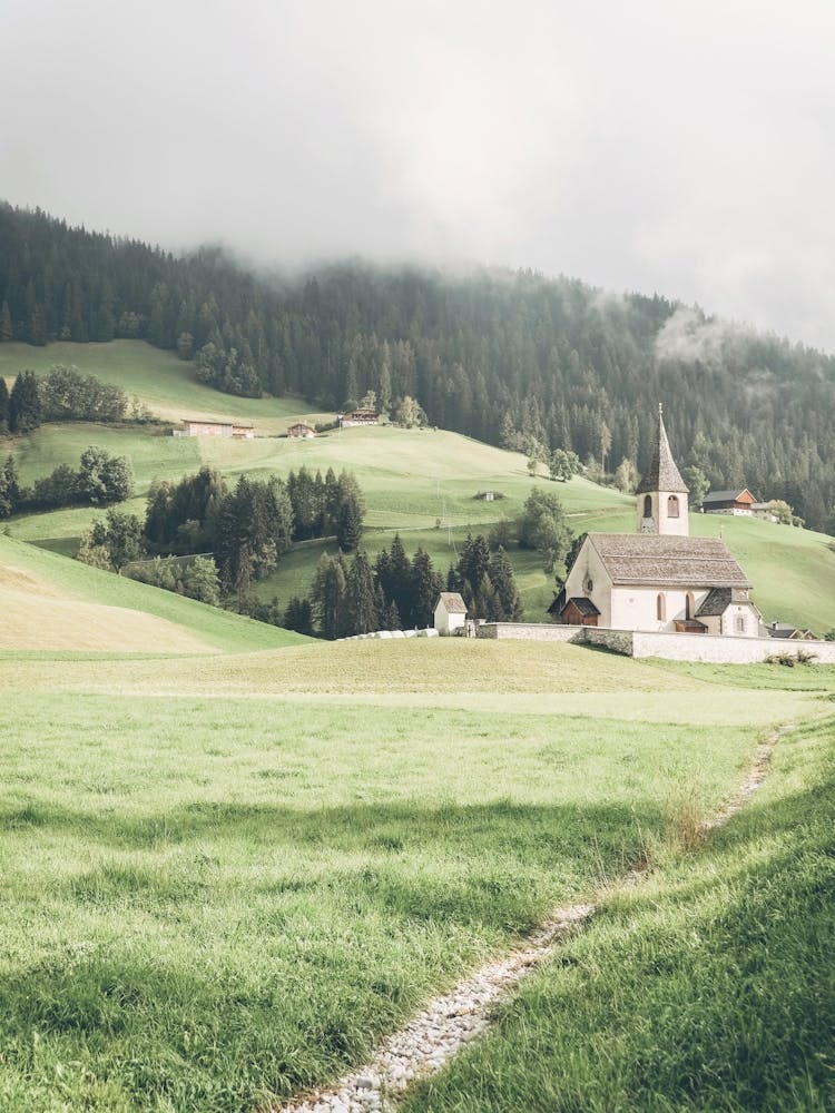 Dolomites, Italy I Mountain church in the heart of nature Alps landscape photography beside Lake Lago di Braies between green hills majestic fir trees and a mysterious mist with a dark moody aesthetic vibes