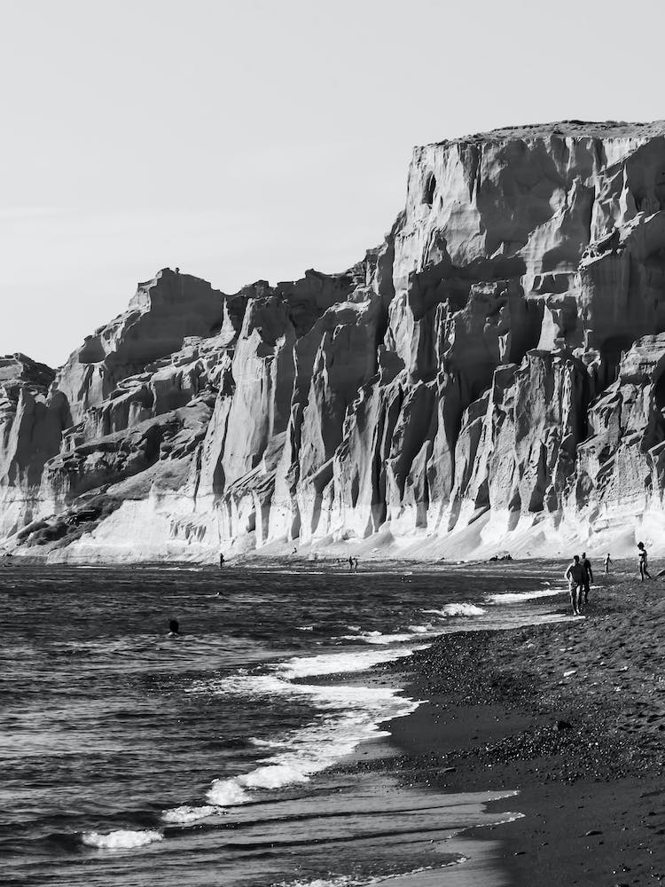 Zerklüftete Meeresklippen und sanfte Wellen an einem Strand auf Santorin