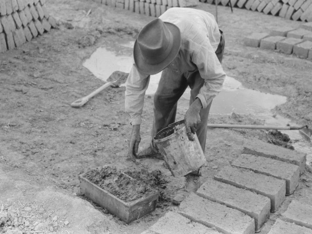 Adding A Little Water To Adobe Mixture In Wooden Form In Process Of Making Adobe Bricks, Chamisal, New Mexico