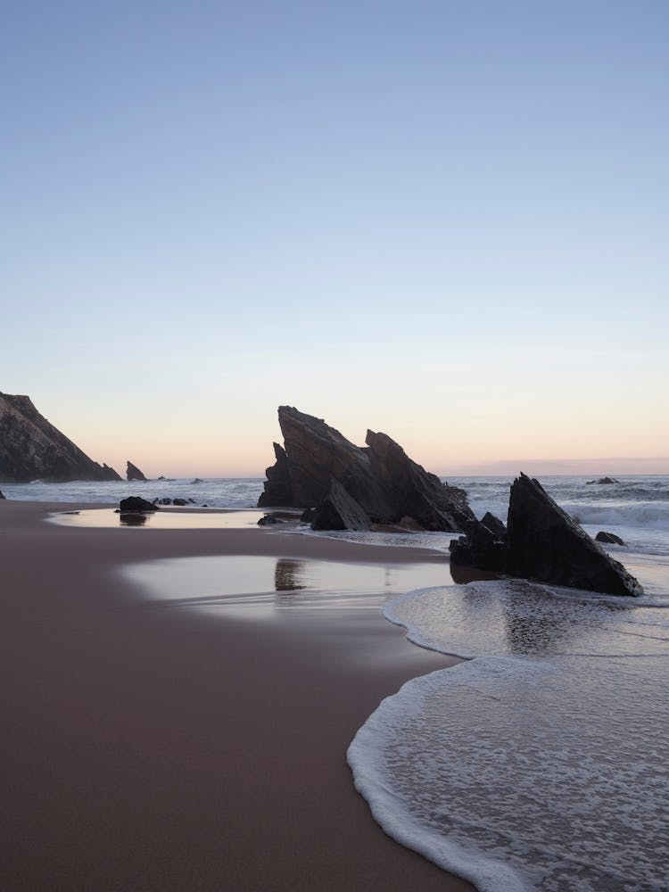 Rocks at Praia da Adraga at sunrise - pink sky on a beach in Portugal summer nature and travel photography by Christa Stroo.
