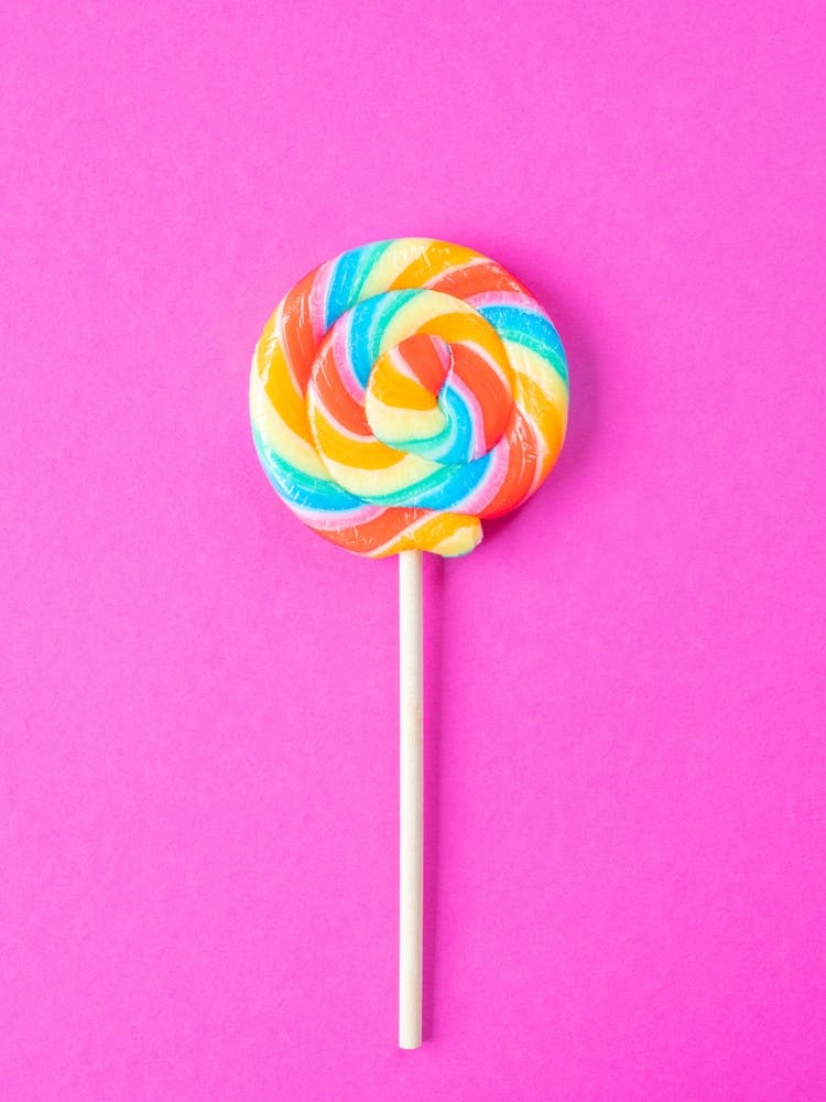 Regenbogenfarbener Lolly auf leuchtend rosa Hintergrund – Food-Fotografie ideal für ein Kinderzimmer von Christa Stroo Photography