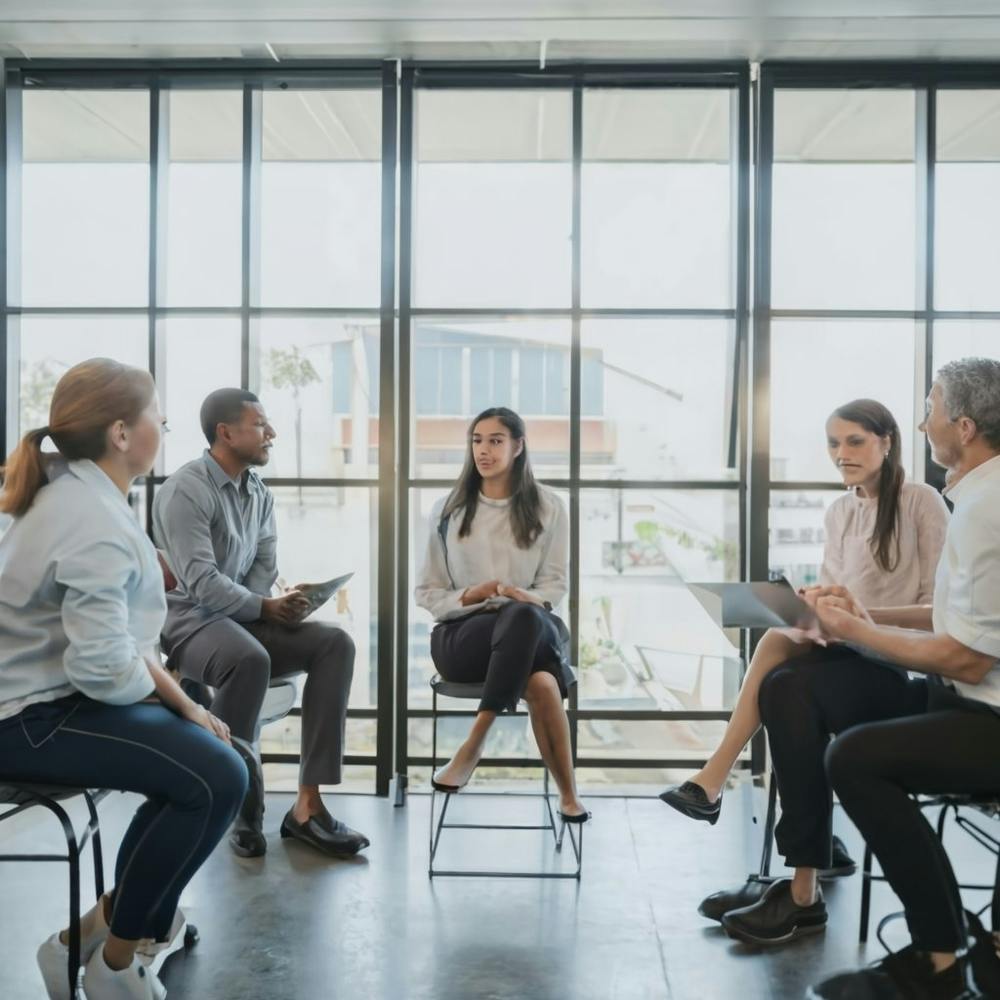 An expressive and diverse group of employees engaged in a casual, yet professional, meeting or discussion in a modern office space. This image communicates collaboration, diversity, and a positive work environment, suitable for various business-related applications