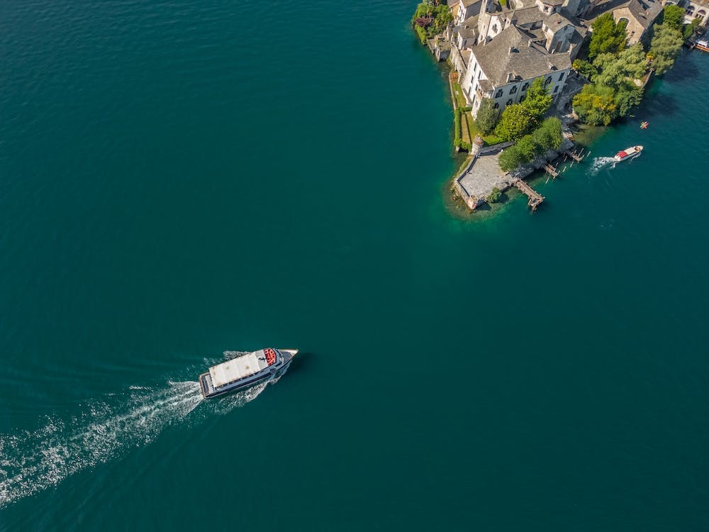 The boat sails to the island on the lake in Italy. Drone photography